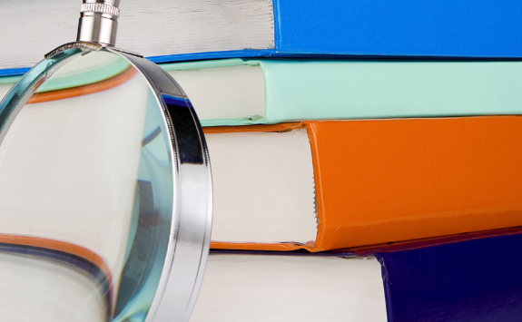 Stack of different coloured books with a magnifying glad resting against them